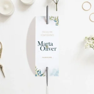 Bengala de boda personalizada con los nombres 'Marta & Oliver' y un diseño floral en tonos azules y verdes, colocada sobre una mesa decorada con velas y flores blancas.