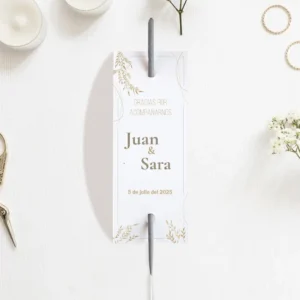 Etiqueta para bengalas de boda con diseño elegante en blanco y detalles dorados, personalizada con los nombres Juan & Sara y la fecha del evento, colocada sobre una mesa decorada con velas y flores.