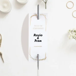 Etiqueta para bengalas de boda con diseño elegante en blanco y detalles dorados, personalizada con los nombres Rocío & Fran y la fecha del evento, colocada sobre una mesa decorada con velas y flores.