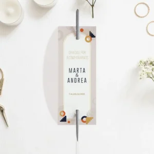 Etiqueta para bengalas de boda con diseño art déco en tonos beige, azul marino y dorado, con los nombres de Marta & Andrea y la fecha del evento, colocada sobre una mesa con velas y flores decorativas.