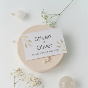 Tarjeta de cuenta bancaria para regalo de boda con los nombres 'Stiven & Oliver' y número IBAN, decorada con detalles dorados de hojas en un diseño elegante y minimalista, sobre fondo claro con flores blancas.