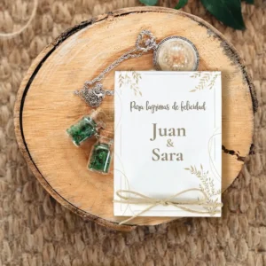 Detalle de boda rústico con tarjeta personalizada que dice 'Para lágrimas de felicidad - Juan & Sara', decorada con lazo de yute. Acompañada de colgantes con frascos de cristal y detalles naturales sobre una base de madera.