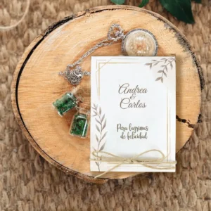 Detalle de boda rústico con tarjeta personalizada que dice 'Andrea & Carlos - Para lágrimas de felicidad', decorada con lazo de yute. Acompañada de colgantes con frascos de cristal y detalles naturales sobre una base de madera.