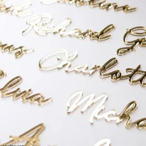 Nombres personalizados en acrílico dorado con tipografía elegante, ideales como marcasitios para bodas y eventos especiales, dispuestos sobre fondo blanco.