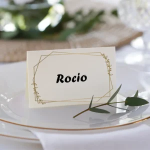 Tarjeta de lugar para boda con el nombre 'Rocío', diseño minimalista con detalles dorados, colocada sobre un plato blanco con borde dorado y decorada con una ramita de olivo.