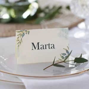 Tarjeta de lugar para boda con el nombre 'Marta', diseño floral en tonos verdes y azules, colocada sobre un plato blanco con borde dorado y decorada con una ramita de olivo.