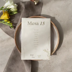 Tarjeta de asignación de mesa para boda con diseño minimalista en tonos beige y dorado, con nombres de los invitados y detalles sutiles, colocada sobre un plato de cerámica con decoración en tonos neutros y flores frescas.