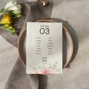Tarjeta de asignación de mesa para boda con diseño floral en tonos pastel, con nombres de los invitados y detalles románticos, colocada sobre un plato de cerámica con decoración en tonos neutros y flores frescas.