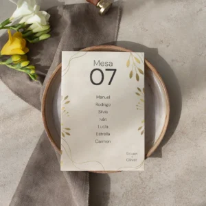 Tarjeta de asignación de mesa para boda con diseño minimalista en tonos beige y dorado, con nombres de los invitados, colocada sobre un plato de cerámica con decoración en tonos neutros y flores frescas