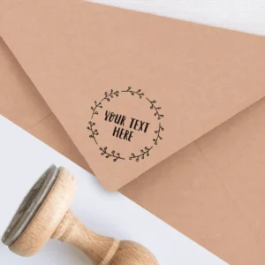 Sello de caucho con diseño floral y texto personalizable, estampado en tinta negra sobre un sobre kraft, acompañado de un sello de madera.