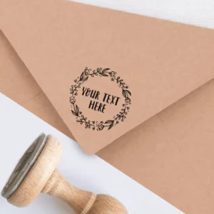 Sello de caucho con diseño floral y texto personalizable, estampado en tinta negra sobre un sobre kraft, acompañado de un sello de madera.