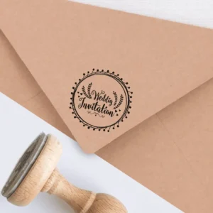Sello de caucho con la frase 'Wedding Invitation' y detalles florales, estampado en tinta negra sobre un sobre kraft, acompañado de un sello de madera.