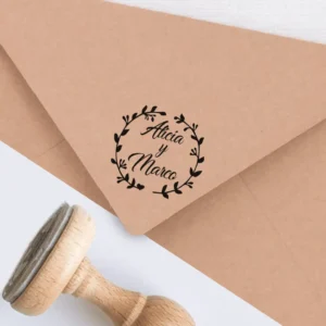 Sello personalizado para bodas con diseño floral, estampado en un sobre kraft. Presenta los nombres 'Alicia y Marco' rodeados de una corona de hojas y ramas.