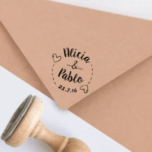 Sello personalizado para bodas con diseño romántico, estampado en un sobre kraft. Incluye los nombres 'Alicia & Pablo', la fecha '23.7.16' y detalles decorativos de corazones.