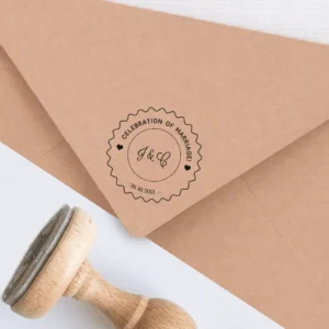 Sello de caucho con la frase 'Celebration of Marriage', personalizado con las iniciales 'J & C' y la fecha del evento, estampado en tinta negra sobre un sobre kraft, junto a un sello de madera.