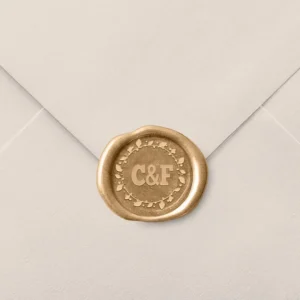 Sello de lacre dorado con diseño personalizado de iniciales 'C & F' rodeadas de un detalle floral, decorando el cierre de un sobre de invitación de boda en color beige.