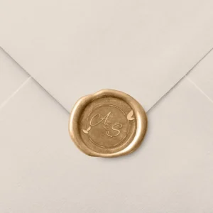 Sello de lacre dorado con diseño elegante personalizado con las iniciales 'A & S' y detalles de hojas, decorando el cierre de un sobre de invitación de boda en color beige.