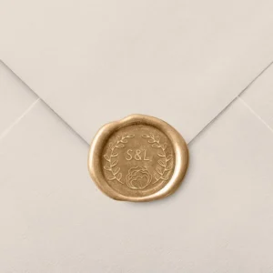 Sello de lacre en tono dorado con diseño personalizado de iniciales 'S&L' y detalles florales, decorando el cierre de un sobre de invitación de boda en color beige.